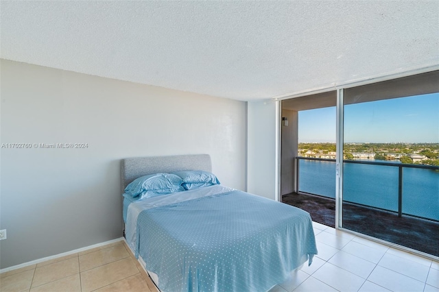 tiled bedroom with access to outside, a textured ceiling, a water view, and floor to ceiling windows