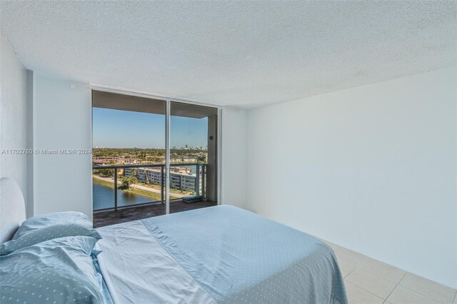 tiled bedroom featuring access to outside, a water view, expansive windows, and a textured ceiling