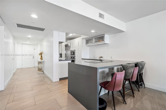 kitchen featuring white cabinets, a kitchen bar, kitchen peninsula, and appliances with stainless steel finishes