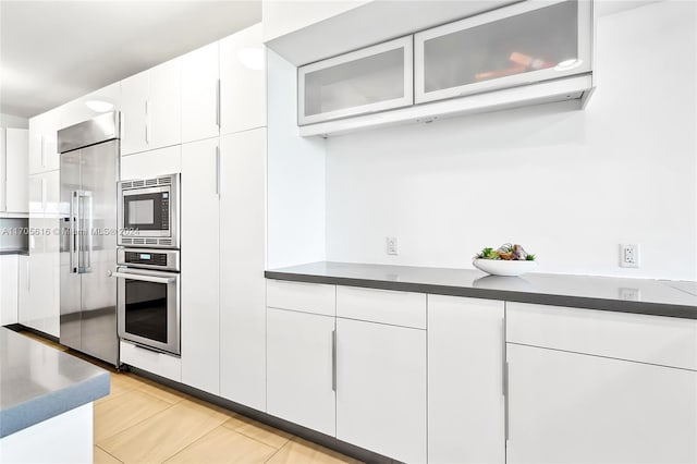 kitchen featuring white cabinets, built in appliances, and light tile patterned flooring