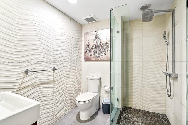 bathroom featuring a tile shower, tile patterned floors, toilet, vanity, and tile walls