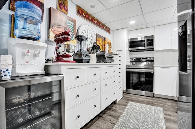 kitchen with white cabinets, a paneled ceiling, stainless steel appliances, and hardwood / wood-style flooring