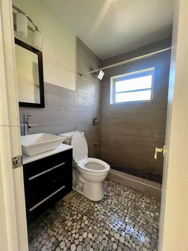 bathroom with vanity, tiled shower, tile walls, tile patterned flooring, and toilet