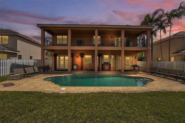 pool at dusk featuring french doors, a patio, and a lawn