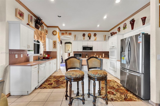 kitchen featuring crown molding, a breakfast bar, white cabinets, and appliances with stainless steel finishes