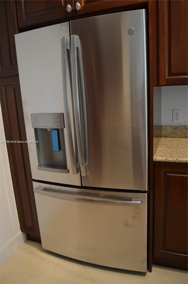 kitchen with stainless steel fridge with ice dispenser, light stone counters, dark brown cabinets, and light tile patterned flooring