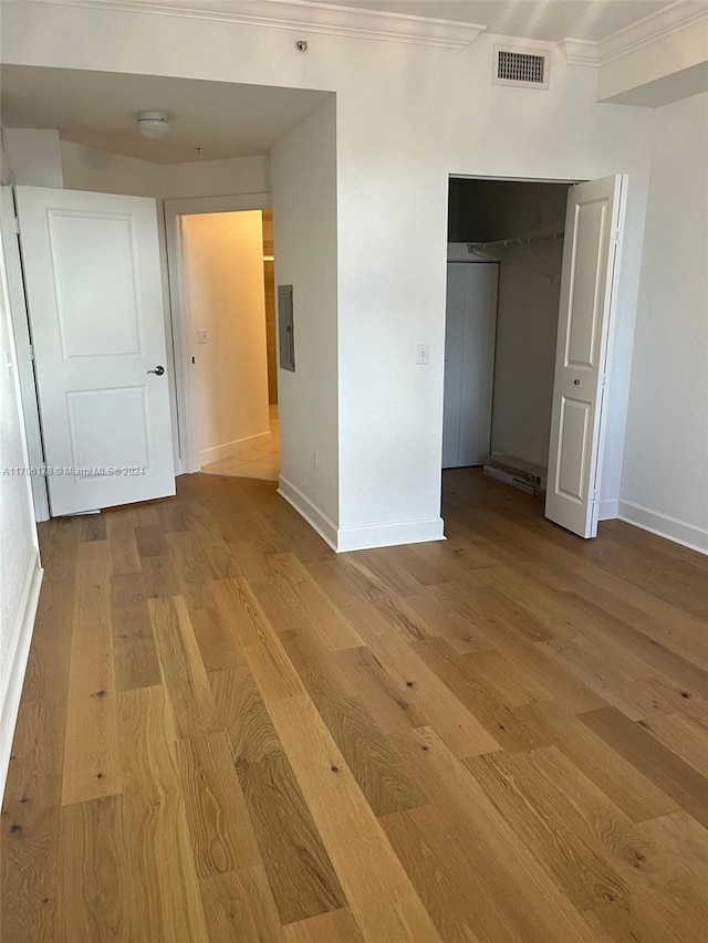 unfurnished bedroom featuring light hardwood / wood-style floors, crown molding, electric panel, and a closet