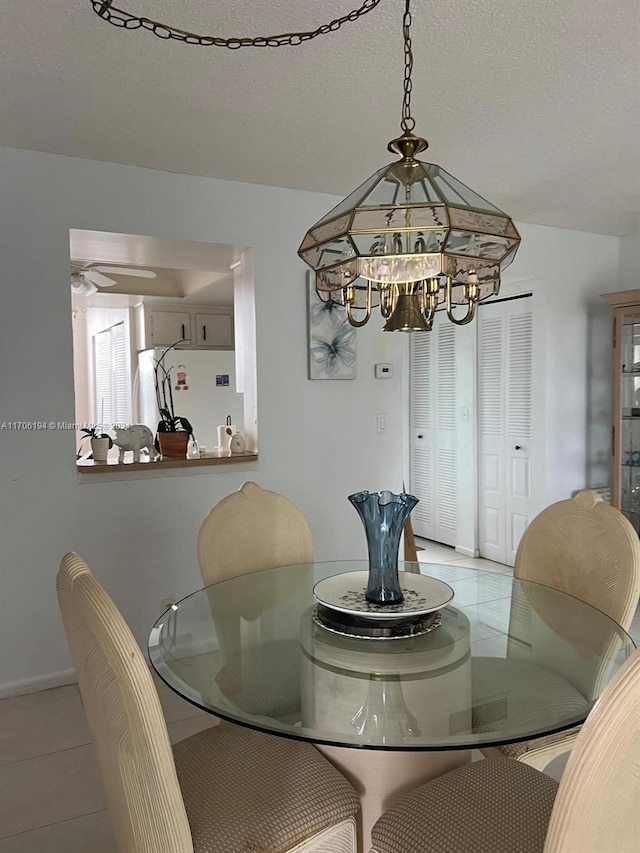 tiled dining area featuring a textured ceiling and ceiling fan with notable chandelier