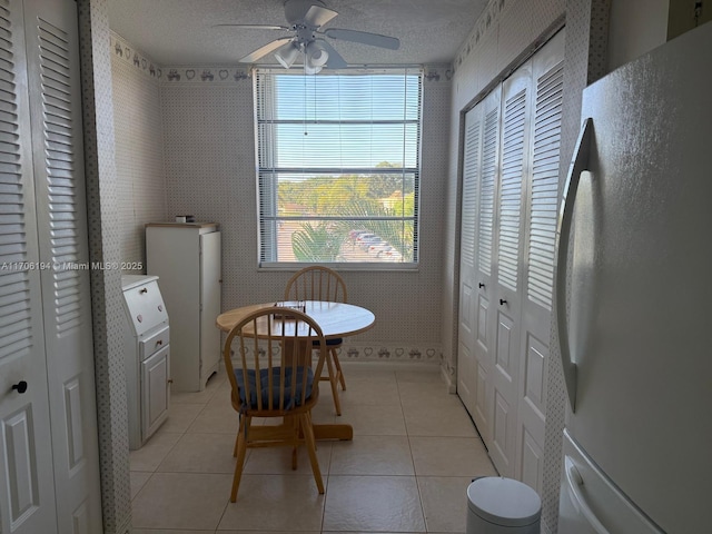 dining room featuring light tile patterned floors, ceiling fan, wallpapered walls, and a textured ceiling