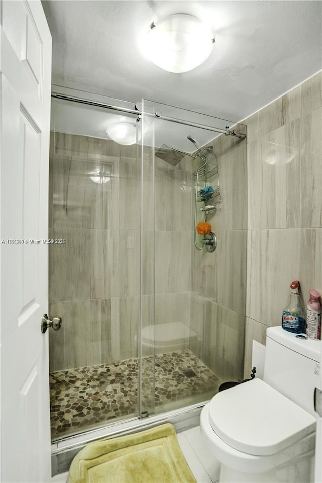 bathroom with tile patterned flooring, toilet, and a shower with door