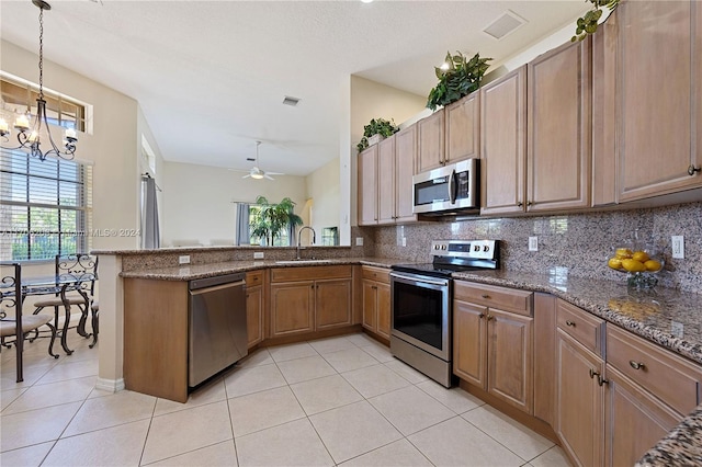 kitchen featuring dark stone counters, sink, decorative light fixtures, kitchen peninsula, and stainless steel appliances