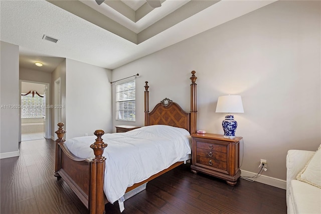 bedroom with a textured ceiling, ceiling fan, dark wood-type flooring, and connected bathroom