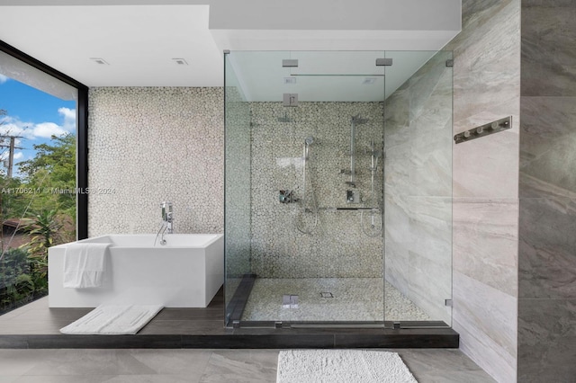 bathroom with expansive windows, tile walls, and separate shower and tub