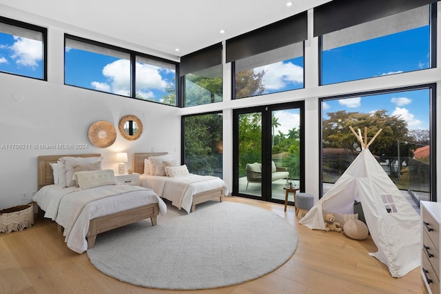 bedroom featuring access to exterior, a towering ceiling, light hardwood / wood-style floors, and a wall of windows