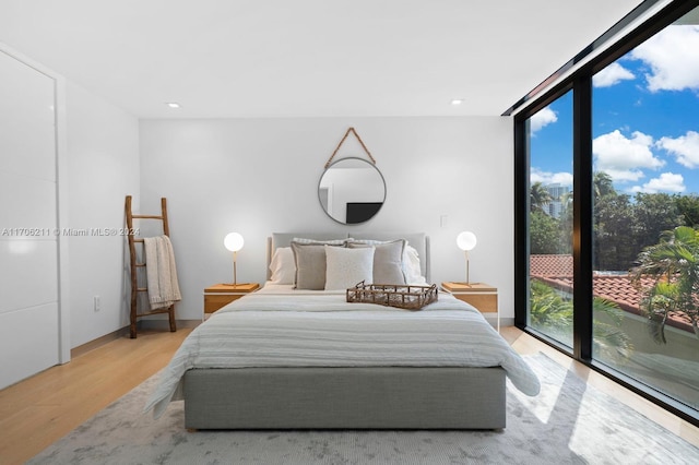 bedroom featuring access to outside, a wall of windows, light hardwood / wood-style floors, and multiple windows