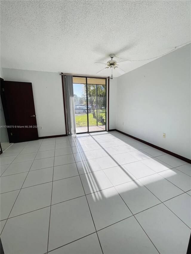 tiled empty room with ceiling fan, expansive windows, and a textured ceiling