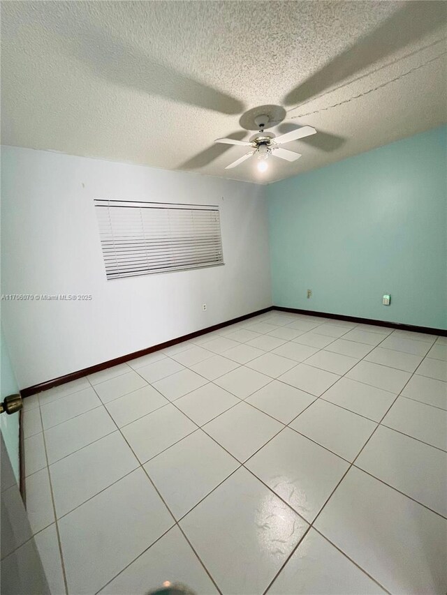 empty room with ceiling fan, light tile patterned floors, and a textured ceiling