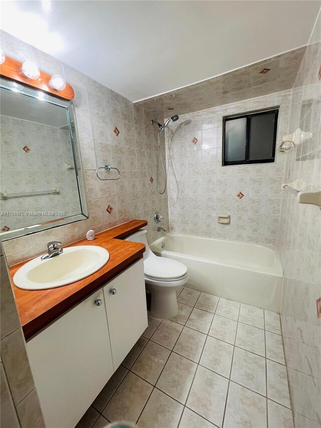 full bathroom with vanity, tile patterned flooring, tiled shower / bath combo, toilet, and tile walls