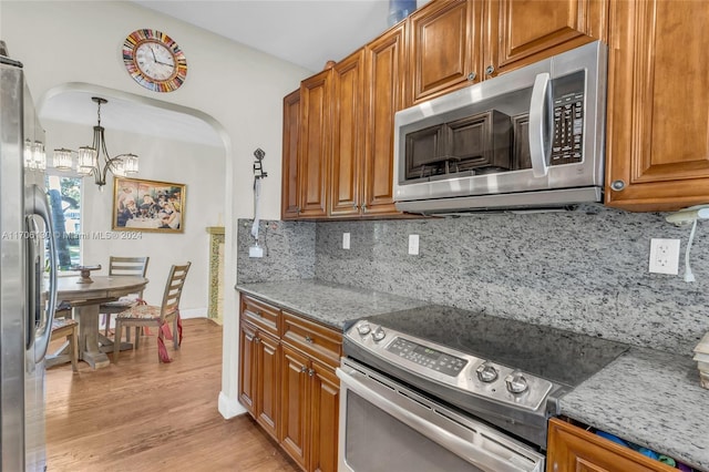 kitchen with a notable chandelier, light stone countertops, backsplash, and appliances with stainless steel finishes