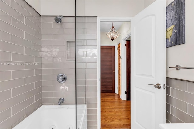 bathroom with wood-type flooring, tiled shower / bath, and an inviting chandelier