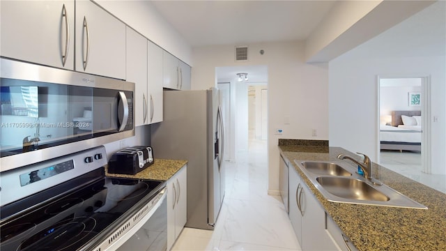 kitchen with sink, white cabinetry, stainless steel appliances, and dark stone counters