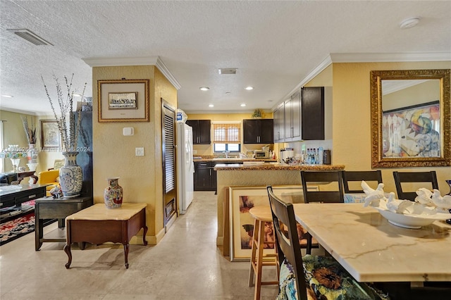 kitchen featuring a kitchen bar, dark brown cabinets, a textured ceiling, and crown molding