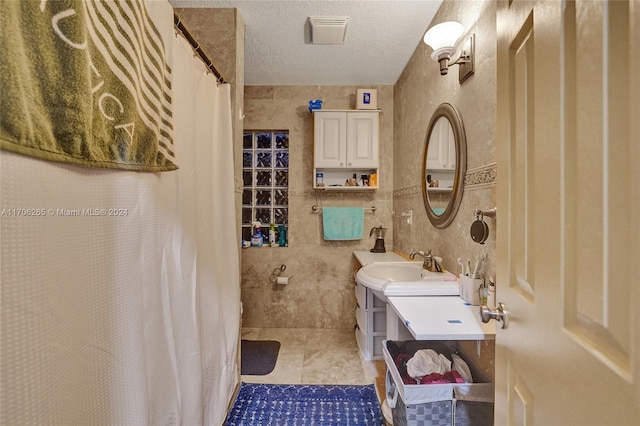 bathroom featuring tile patterned flooring, a textured ceiling, vanity, and tile walls