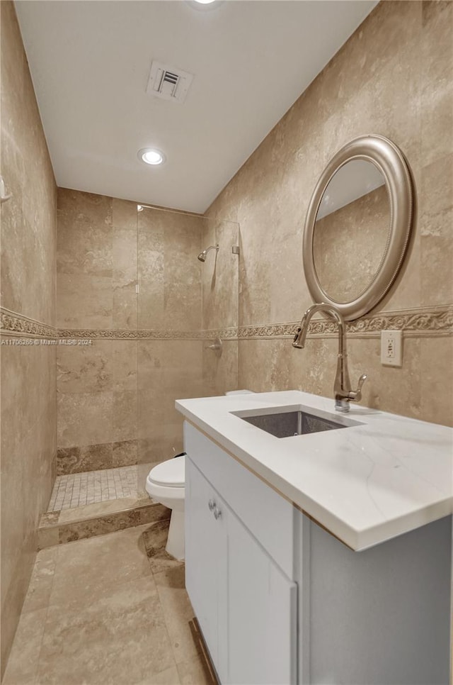 bathroom featuring vanity, toilet, tiled shower, and tile walls