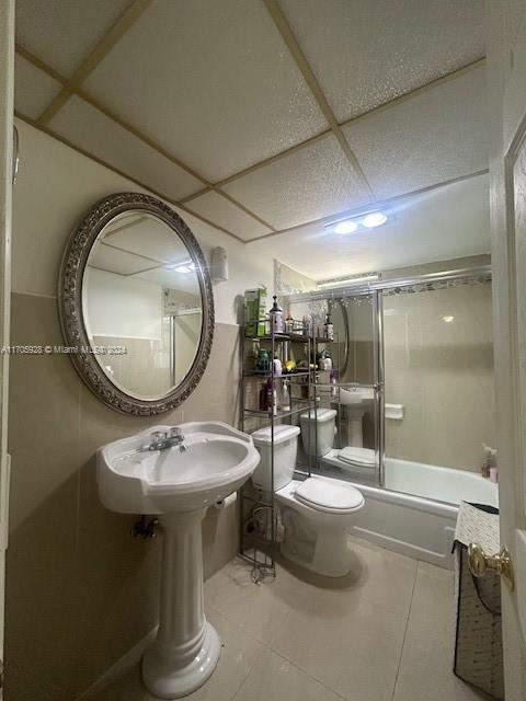 full bathroom featuring a drop ceiling, tile patterned floors, combined bath / shower with glass door, sink, and toilet