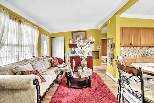 living room featuring lofted ceiling, light hardwood / wood-style flooring, crown molding, and sink