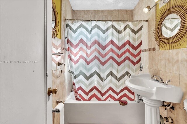 bathroom with a textured ceiling, shower / bathtub combination with curtain, and tile walls