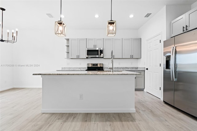 kitchen featuring a kitchen island with sink, stainless steel appliances, and decorative light fixtures