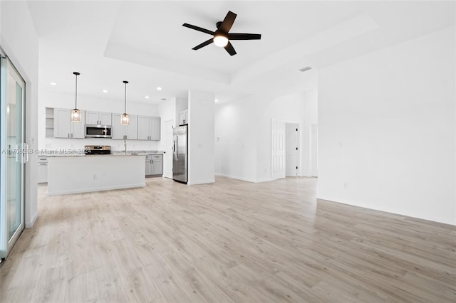 unfurnished living room featuring ceiling fan, light wood-type flooring, sink, and a tray ceiling