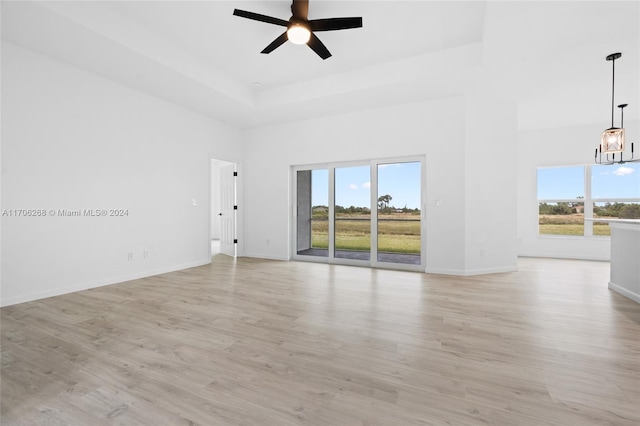 unfurnished room featuring a high ceiling, ceiling fan with notable chandelier, light hardwood / wood-style floors, and plenty of natural light