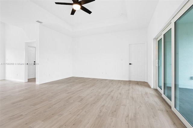 empty room featuring a tray ceiling, ceiling fan, and light hardwood / wood-style floors