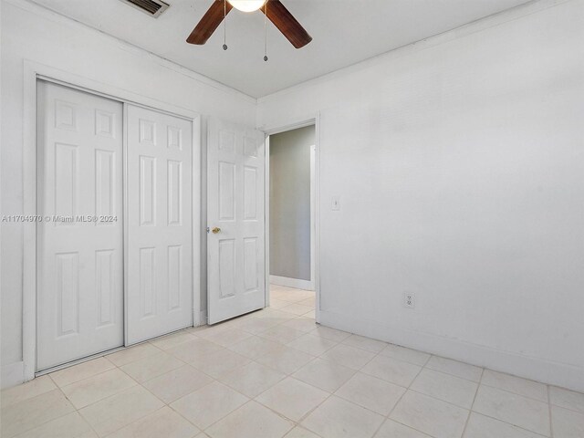 unfurnished bedroom with ceiling fan, light tile patterned floors, ornamental molding, and a closet