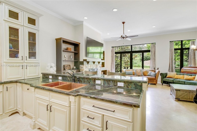 kitchen with ceiling fan, sink, dark stone countertops, crown molding, and cream cabinets