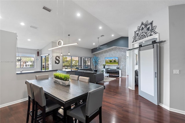 dining space with a barn door, ceiling fan, dark hardwood / wood-style floors, and vaulted ceiling