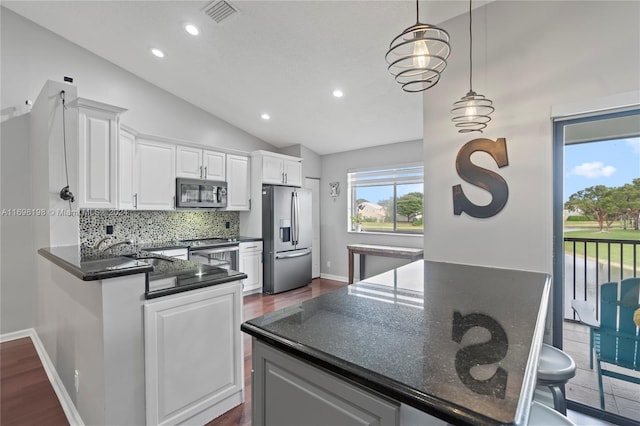 kitchen with dark stone counters, lofted ceiling, decorative light fixtures, white cabinets, and appliances with stainless steel finishes