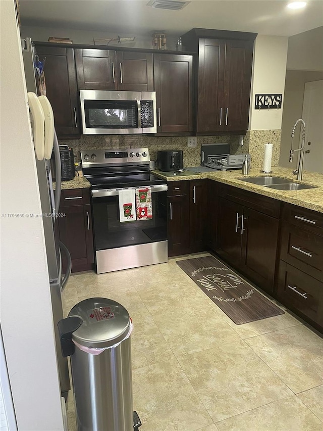 kitchen with light stone countertops, backsplash, dark brown cabinetry, stainless steel appliances, and sink