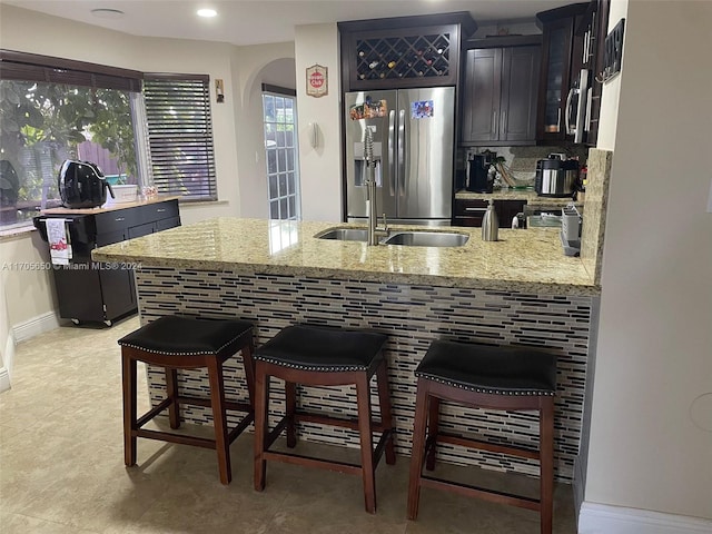 kitchen with kitchen peninsula, stainless steel refrigerator with ice dispenser, a kitchen breakfast bar, light stone counters, and sink