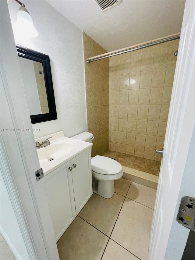 bathroom with tile patterned floors, toilet, a tile shower, and vanity