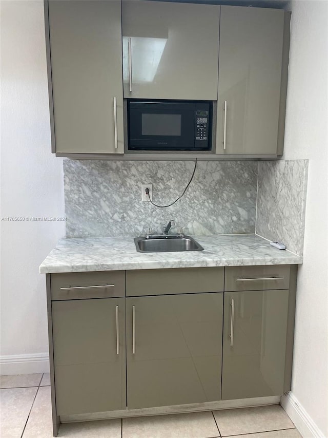 kitchen featuring backsplash, black microwave, sink, and light stone counters