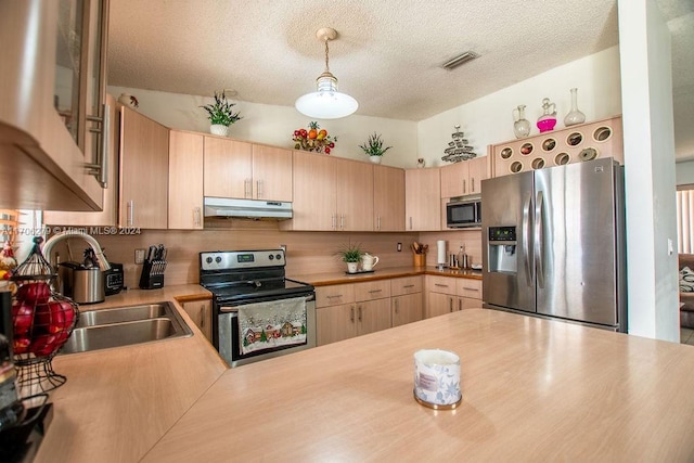 kitchen featuring kitchen peninsula, appliances with stainless steel finishes, light brown cabinetry, a textured ceiling, and hanging light fixtures