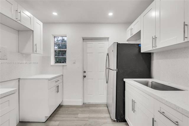 kitchen featuring stainless steel fridge, light wood-type flooring, backsplash, light stone counters, and white cabinets