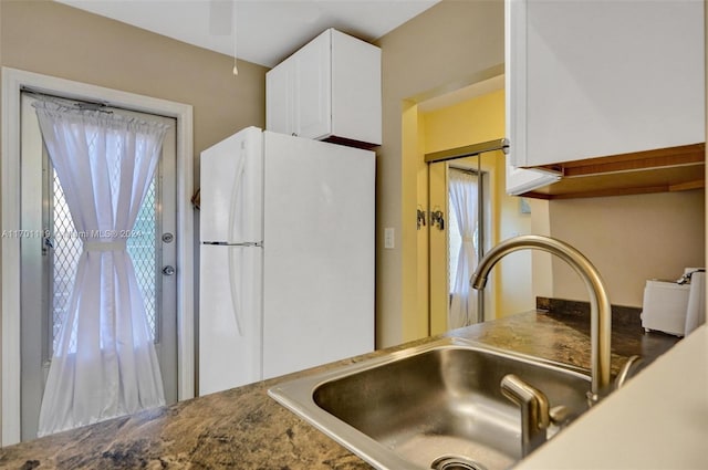 kitchen with a wealth of natural light, white cabinetry, sink, and white fridge