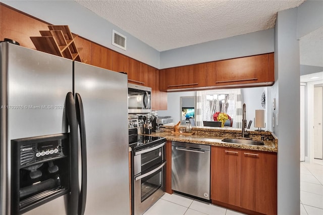 kitchen with sink, a textured ceiling, stone countertops, light tile patterned flooring, and stainless steel appliances