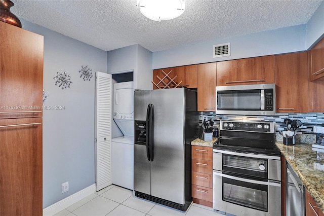 kitchen with decorative backsplash, light tile patterned floors, a textured ceiling, appliances with stainless steel finishes, and stacked washer / drying machine