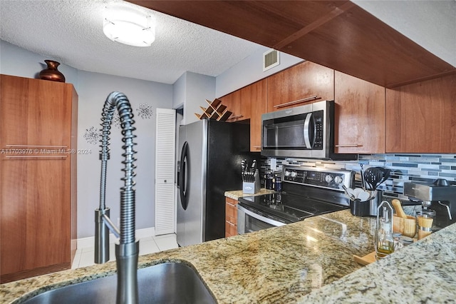 kitchen featuring sink, light tile patterned floors, a textured ceiling, appliances with stainless steel finishes, and tasteful backsplash