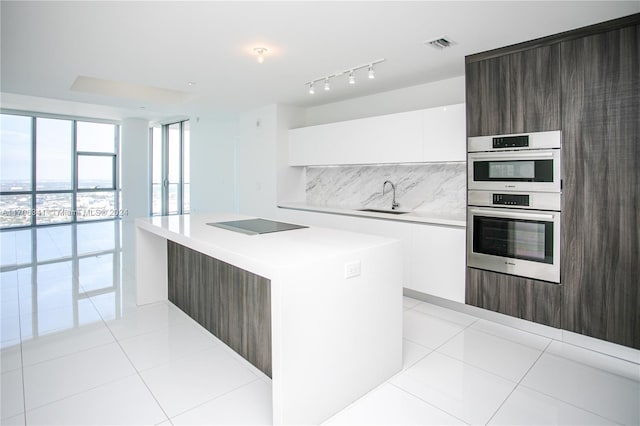 kitchen featuring a center island, sink, stainless steel double oven, light tile patterned floors, and white cabinets